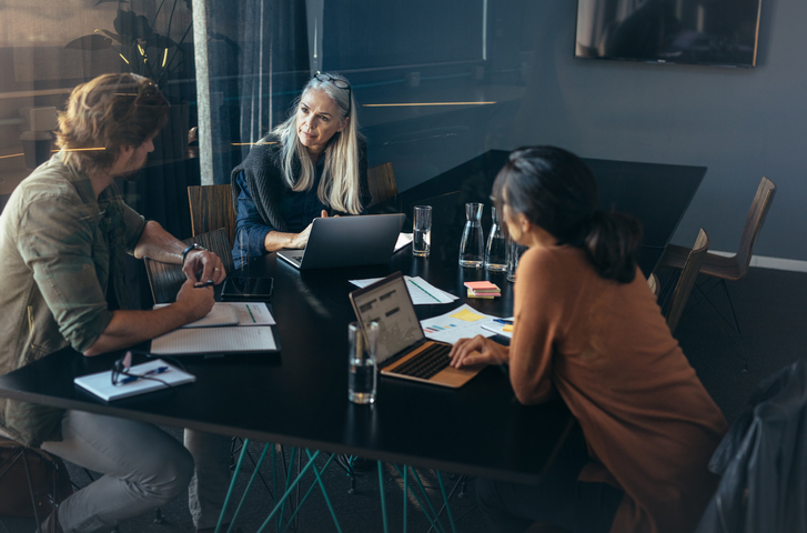 three employees sit around a table holding a conversation