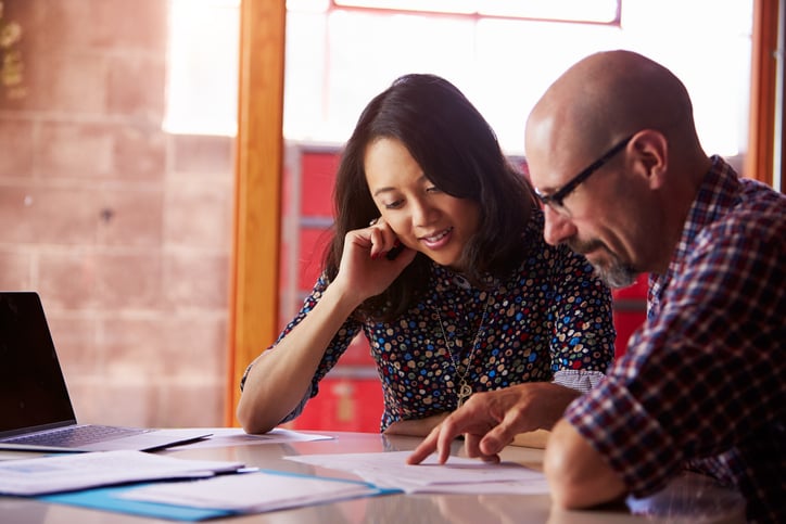 a woman and man sit at a desk working on the same task