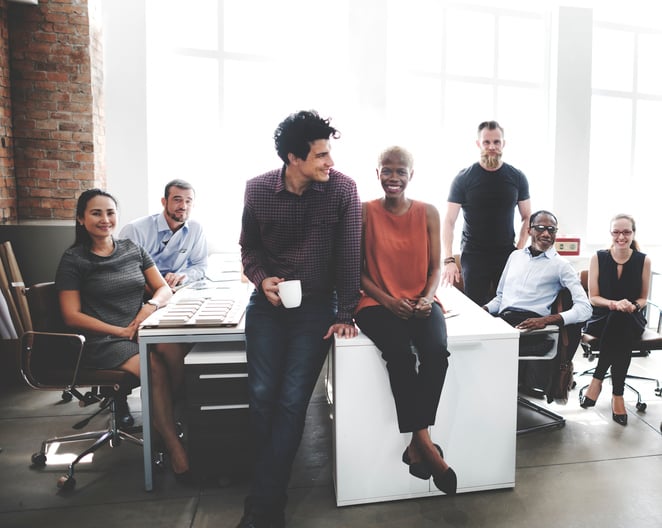 A team of 7 employees sitting on and around a cluster of desks