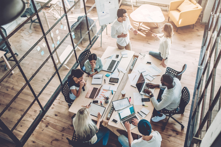 a group of millennial employees sit around a table some working independently, some collaborating