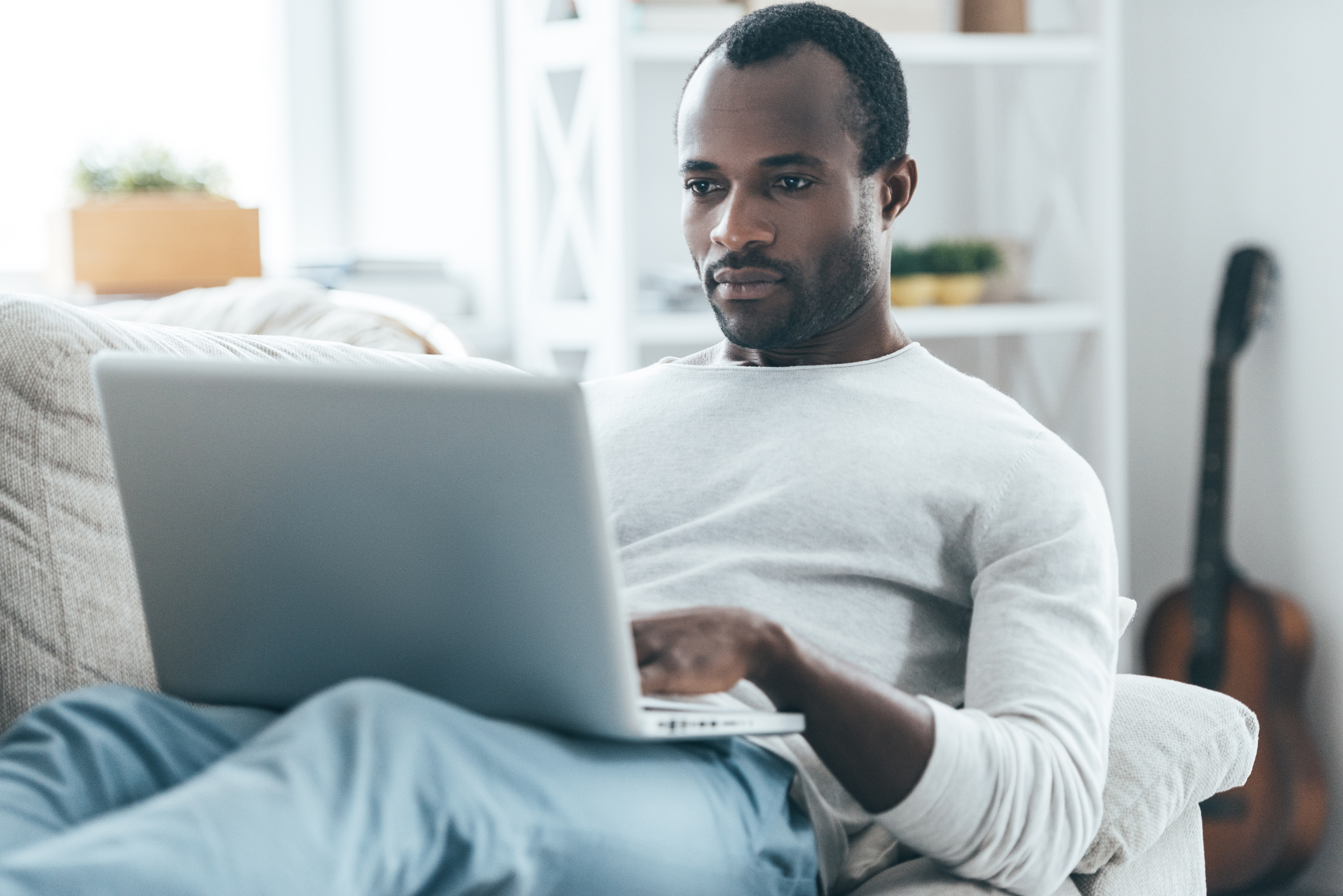 man lounging on sofa looking at laptop