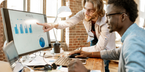 Two colleagues looking at reports on a monitor
